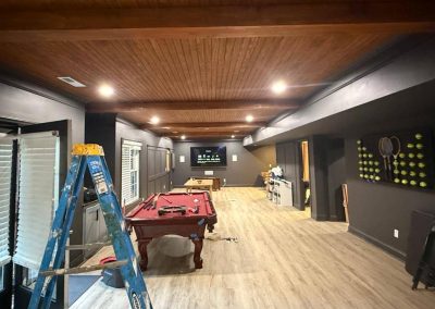 A game room with a pool table, ladder, TV, and tennis ball artwork on a wood floor and ceiling.