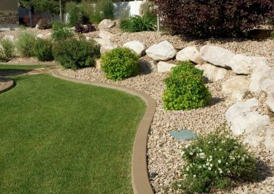 Curved path borders a green lawn with shrubs, rocks, and gravel in a landscaped garden.