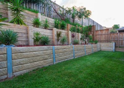 Terraced stone retaining walls with green plants and grass lawn in a backyard garden.
